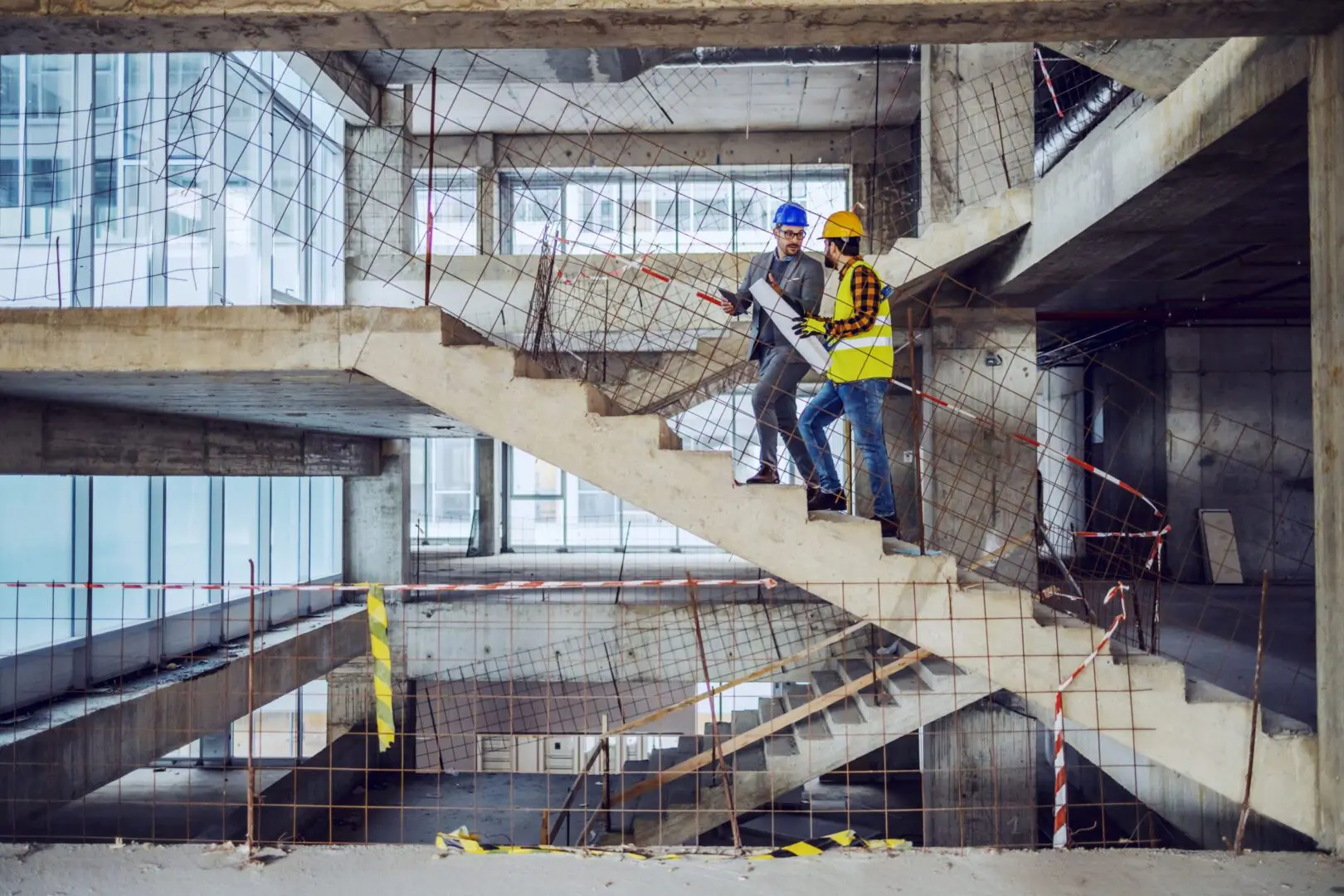 Two men in hard hats and jackets are on a staircase.