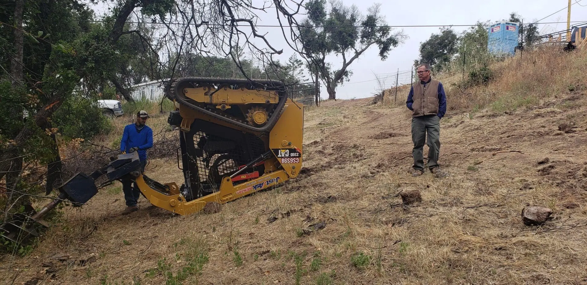 A man standing next to a yellow tractor on top of a hill.